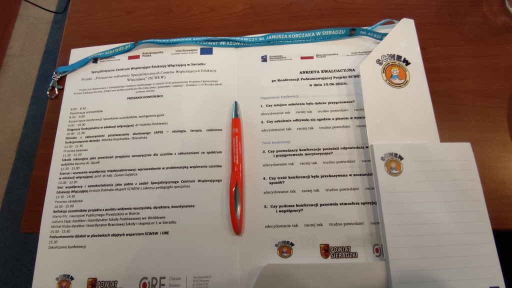 zdjęcie przedstawia komplet materiałów konferencyjnych, który dostawali uczestnicy konferencji w Sieradzu. W skład kompletu wchodzi tecz, program konferencji, długopis, notes i smycz na identyfikator.