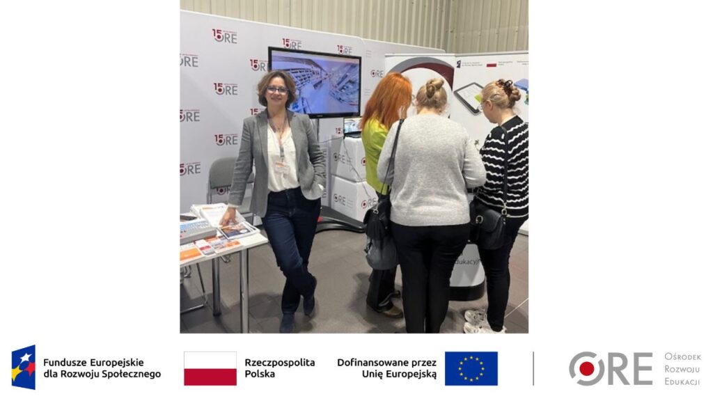 Kierownik projektu Joanna Saska-Dymnicka stoi na tle monitora z wyświetlanym filmem promocyjnym i ścianki z napisem „15-lecie ORE”