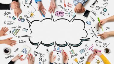 Widok stołu z lotu ptaka. Znajdują się na nim rysunki oraz napisy w języku angielskim. W centralnej części narysowana jest chmura. O stół opierają się dłonie ośmiu osób.