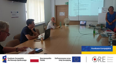 przy stole siedzą eksperci projektu, jedna osoba stoi, w tle na ekranie fragment Standardu technicznego e-materiałów do kształcenia zawodowego