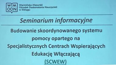 Na zdjęciu widoczny jest wyświetlony z rzutnika slajd z tytułem spotkania „Budowanie skoordynowanego systemu pomocy opartego na Specjalistycznych Centrach Wspierających Edukację Włączającą (SCWEW)”.